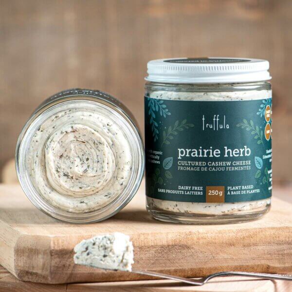 Two Prairie Herb Cultured Cashew Cheese 250g jars, with one placed on its side and the lid off showing the cheese.