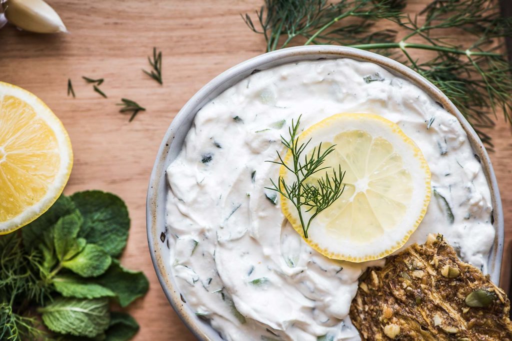 Tzatziki made Truffula cheese, in a bowl on a cutting board. Topped with lemon and dill.